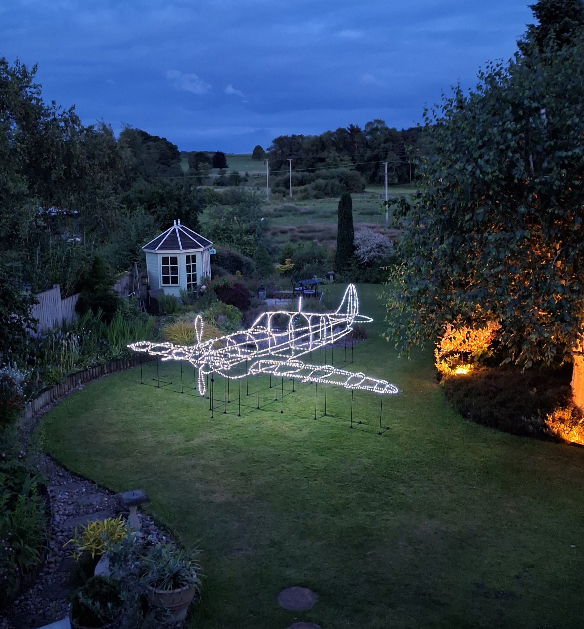 Garden with a large illuminated airplane sculpture at night.